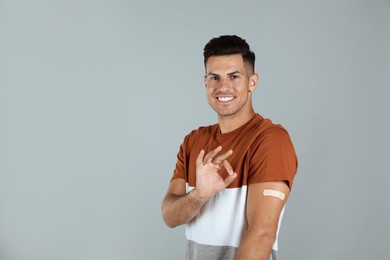 Photo of Vaccinated man with medical plaster on his arm showing okay gesture against grey background
