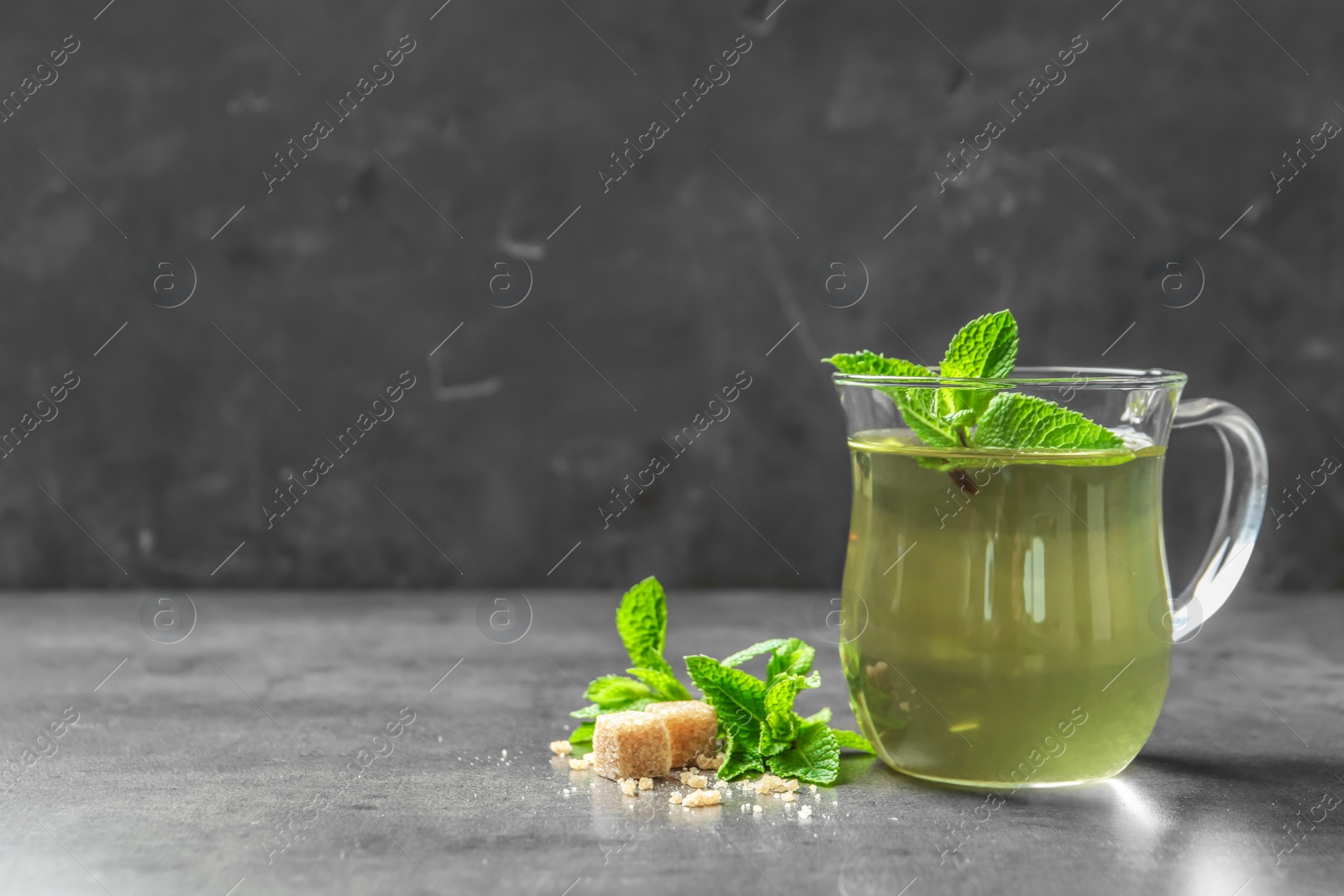 Photo of Cup with hot aromatic mint tea, fresh leaves and sugar cubes on table