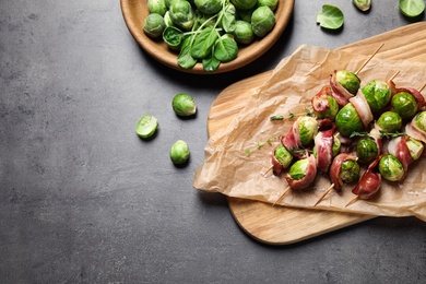 Photo of Skewers with Brussels sprouts and bacon served on grey table, flat lay. Space for text