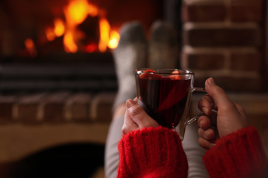 Woman with tasty mulled wine near burning fireplace indoors, closeup