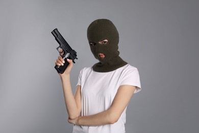 Photo of Woman wearing knitted balaclava with gun on grey background