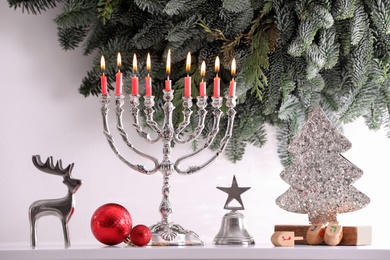Photo of Silver menorah, Christmas decorations and dreidels with symbols He, Nun, Pe, Gimel near fir tree branches. Hanukkah symbol