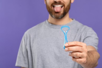 Man with tongue cleaner on violet background, closeup