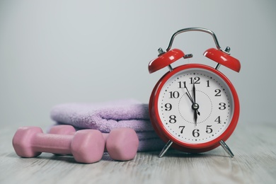 Alarm clock, dumbbells and towel on floor indoors, space for text. Morning exercise