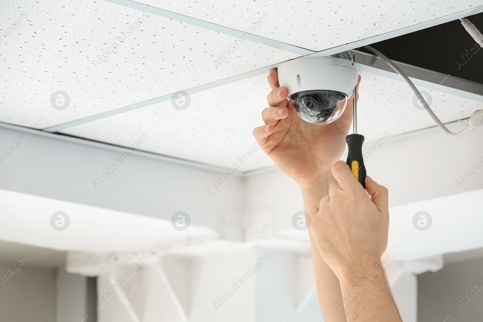 Photo of Technician installing CCTV camera on ceiling indoors, closeup