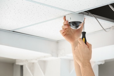 Technician installing CCTV camera on ceiling indoors, closeup