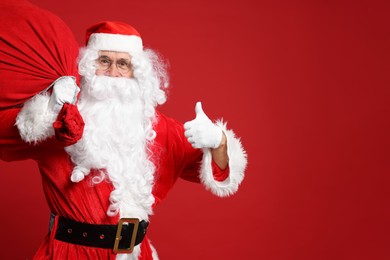 Photo of Santa Claus with bag of Christmas presents showing thumbs up on red background, space for text