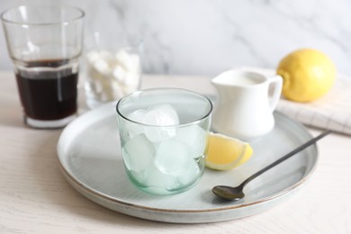 Photo of Making iced coffee. Ice cubes in glass and spoon on white wooden table, closeup