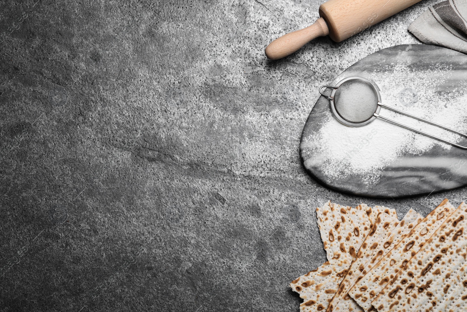 Photo of Traditional matzos, rolling pin and flour on grey table, flat lay. Space for text