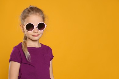 Girl wearing stylish sunglasses on orange background, space for text