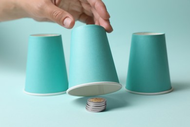 Woman showing coins under cup on light blue background, closeup. Thimblerig game