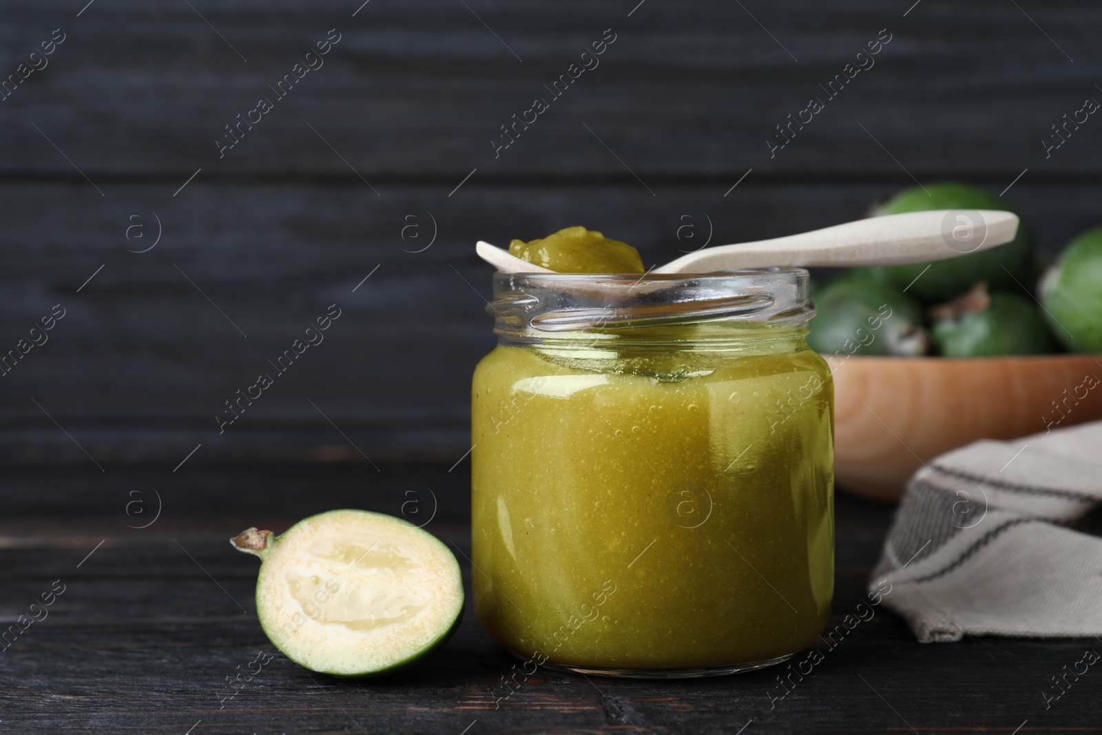 Photo of Feijoa jam and fresh fruit on black wooden table, closeup