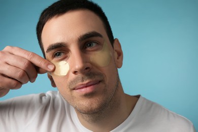 Photo of Young man applying under eye patches on light blue background