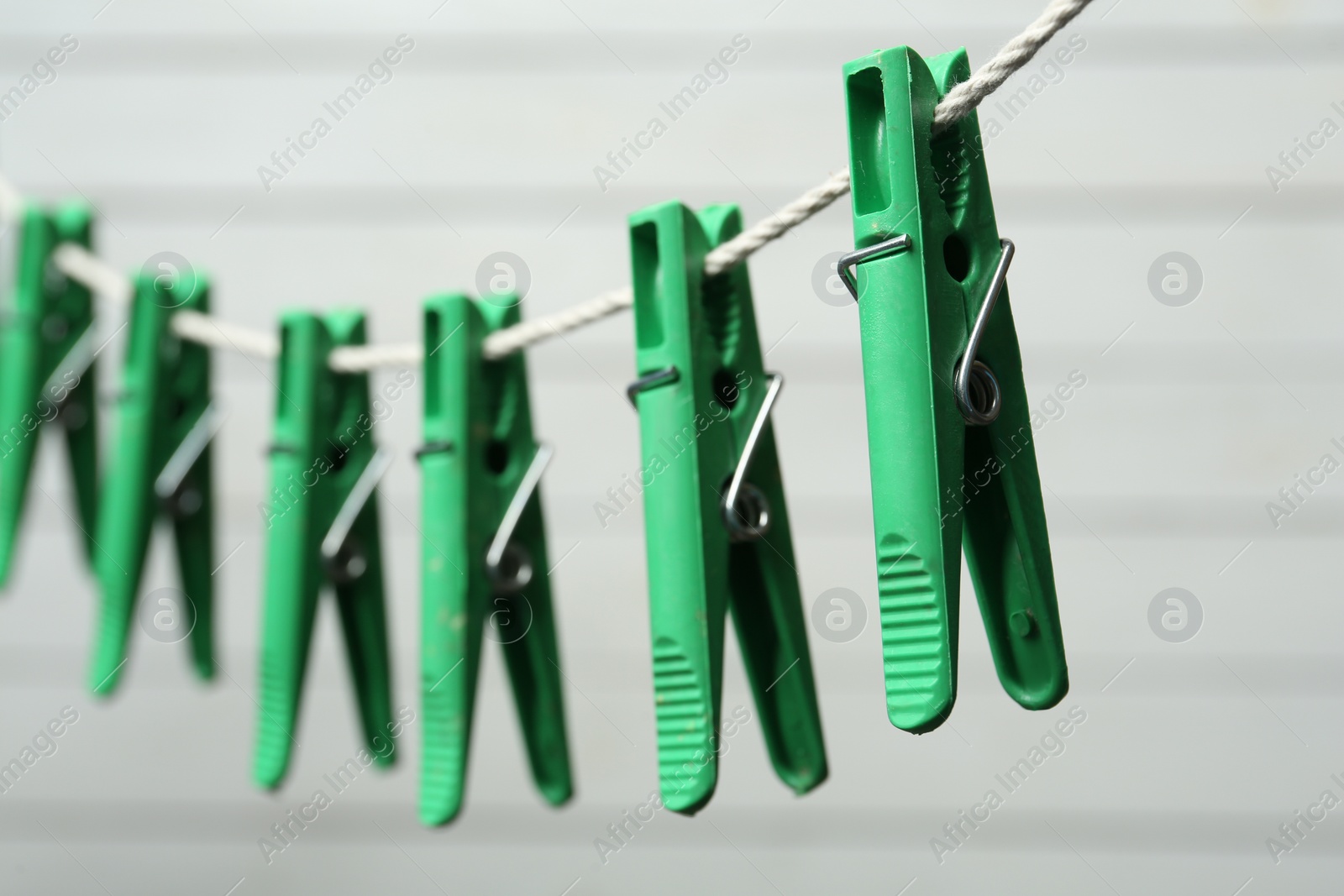 Photo of Green plastic clothespins on rope against light background, closeup