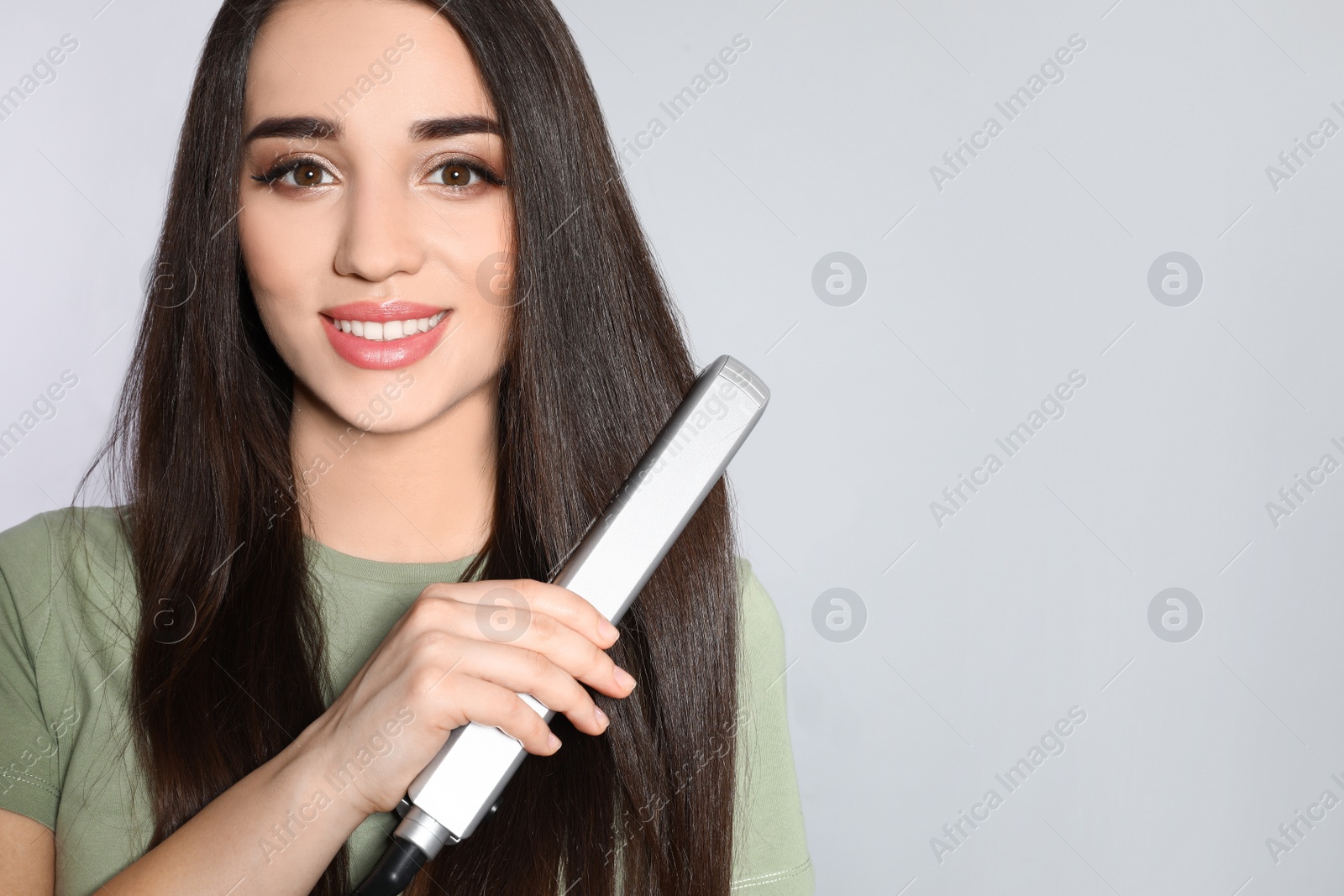 Photo of Happy woman using hair iron on grey background. Space for text