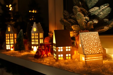 Photo of Christmas atmosphere. Many beautiful glowing houses on window sill indoors