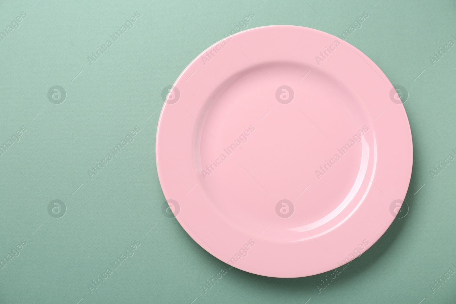 Photo of Empty pink ceramic plate on green background, top view. Space for text