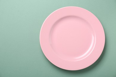 Photo of Empty pink ceramic plate on green background, top view. Space for text