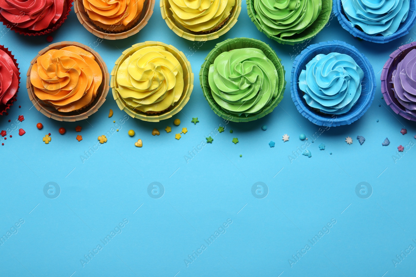 Photo of Many tasty cupcakes with bright cream and sprinkles on light blue background, flat lay. Space for text