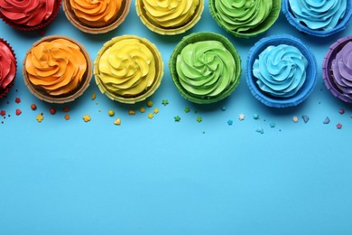 Photo of Many tasty cupcakes with bright cream and sprinkles on light blue background, flat lay. Space for text