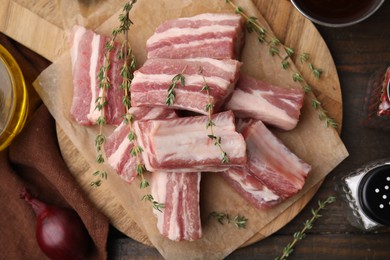 Photo of Cut raw pork ribs with thyme on wooden table, flat lay
