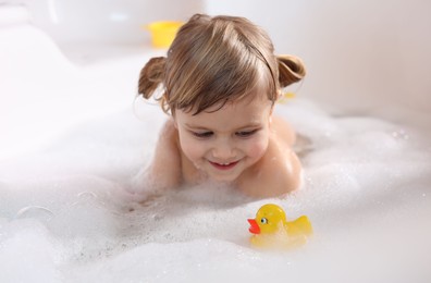 Smiling girl bathing with toy duck in tub