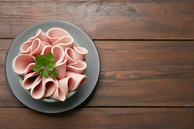 Photo of Slices of delicious boiled sausage with parsley on wooden table, top view. Space for text