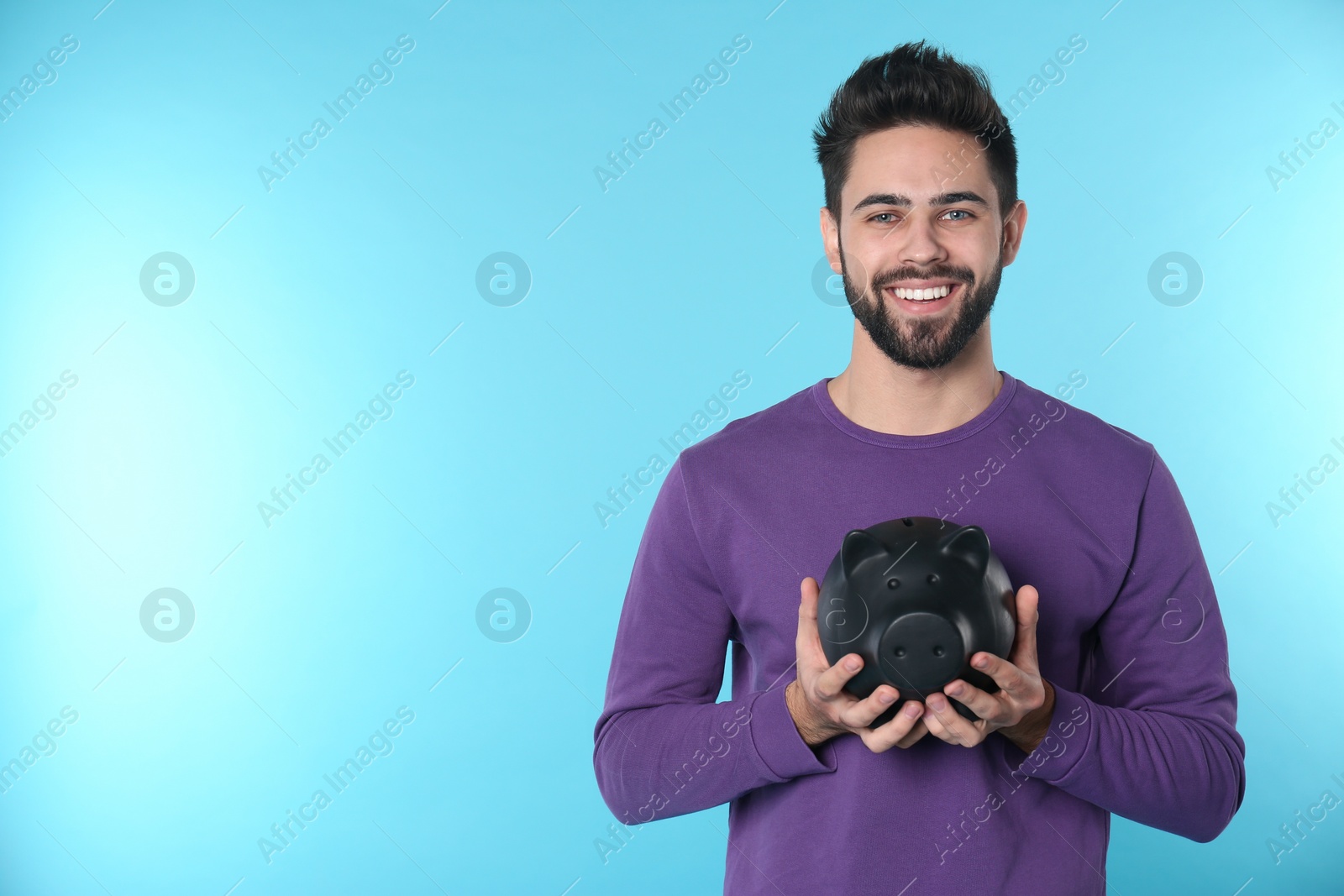 Photo of Happy young man with piggy bank and space for text on color background. Money saving