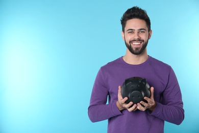 Photo of Happy young man with piggy bank and space for text on color background. Money saving