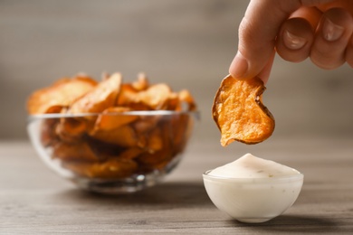 Woman dipping sweet potato chip into sauce on table, closeup. Space for text