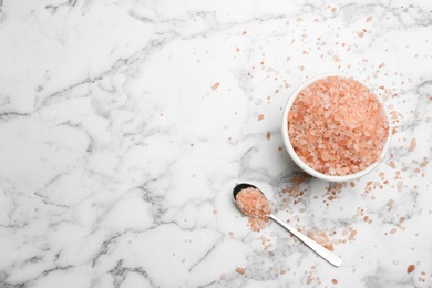 Photo of Spoon and bowl with pink himalayan salt on white marble table, flat lay. Space for text