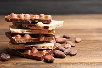 Photo of Yummy chocolate pieces with hazelnuts on wooden table