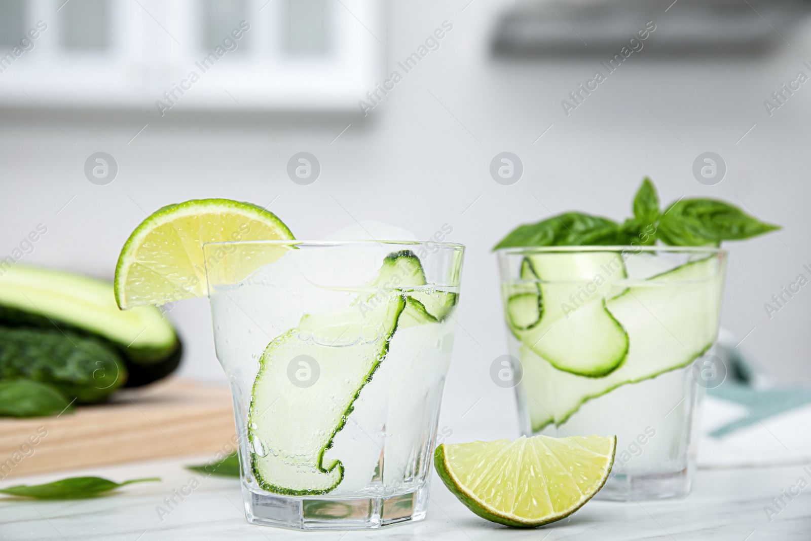 Photo of Tasty fresh cucumber water with sliced lime and basil on white table indoors