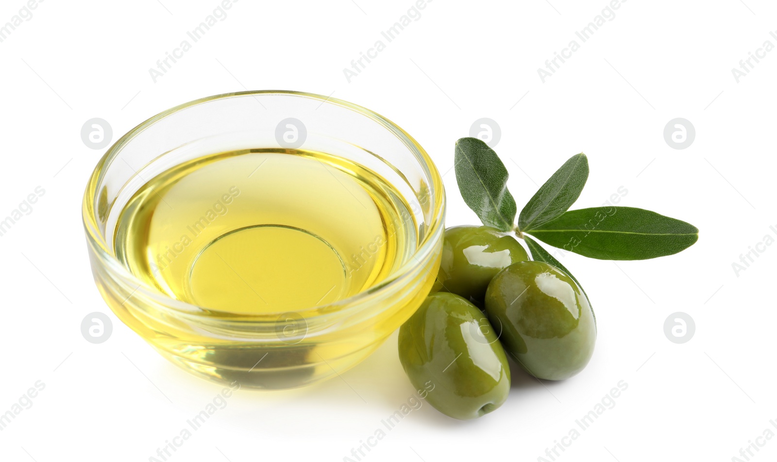 Photo of Glass bowl of oil, ripe olives and green leaves on white background