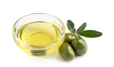 Photo of Glass bowl of oil, ripe olives and green leaves on white background