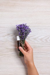 Photo of Woman with bottle of lavender essential oil and flowers on wooden background, closeup