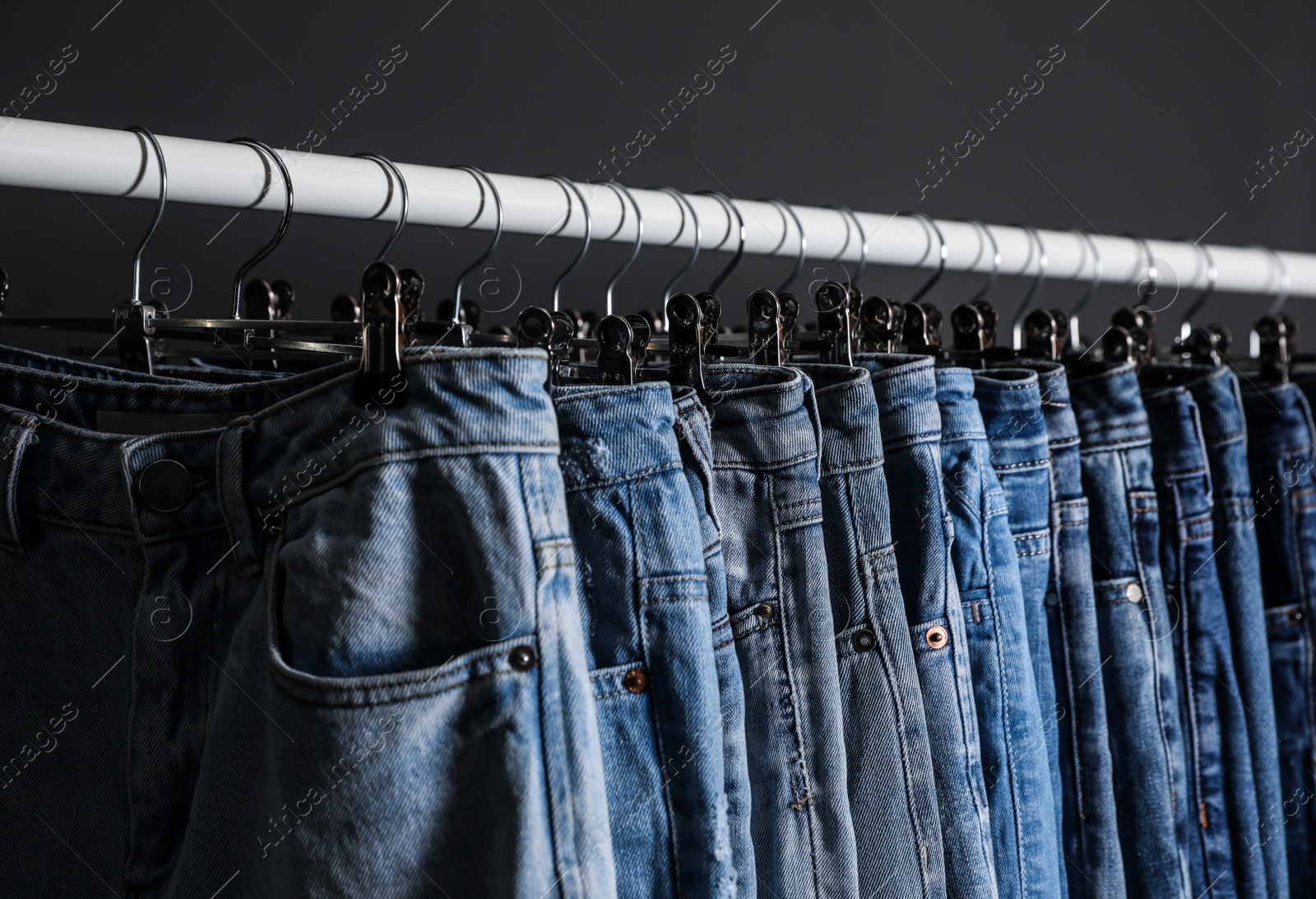 Photo of Rack with different jeans on dark grey background, closeup