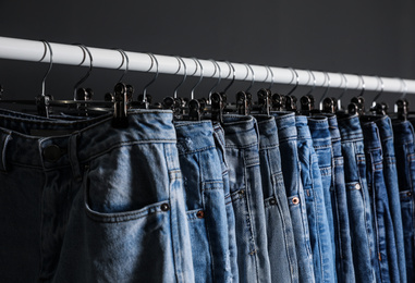 Photo of Rack with different jeans on dark grey background, closeup