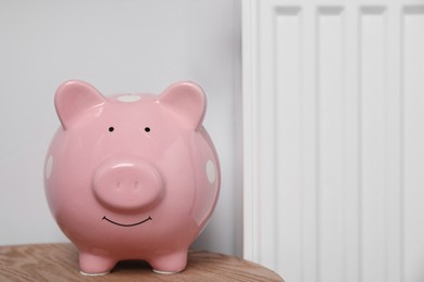 Piggy bank on wooden table near heating radiator, space for text