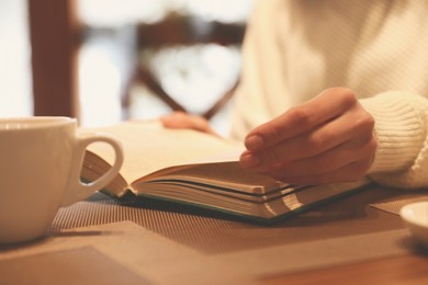 Image of Woman with coffee reading book at wooden table, closeup