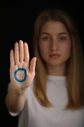 Photo of Woman showing palm with drawn blue circle against black background, focus on hand. World Diabetes Day