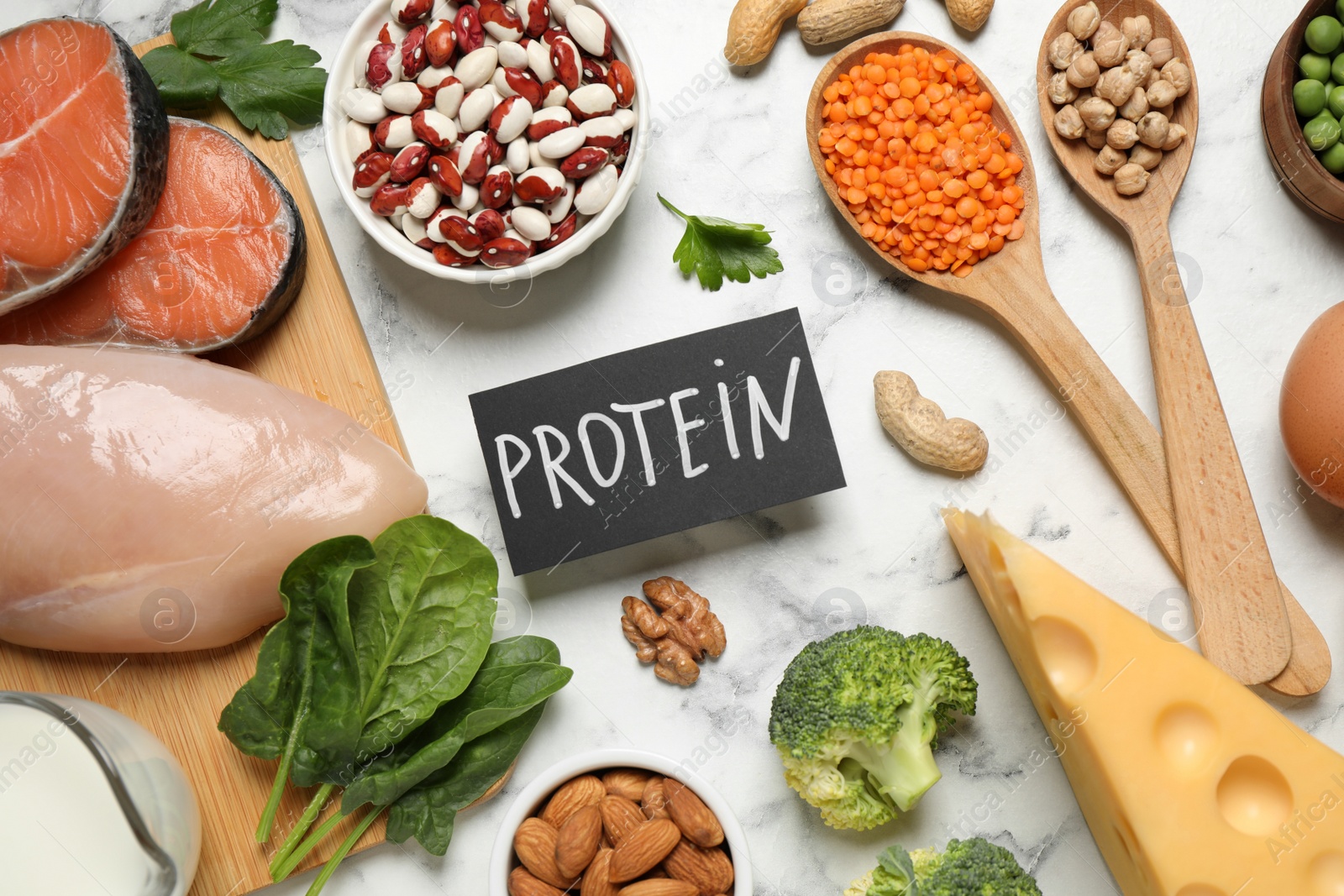 Photo of Card with word PROTEIN and different products on white marble table, flat lay