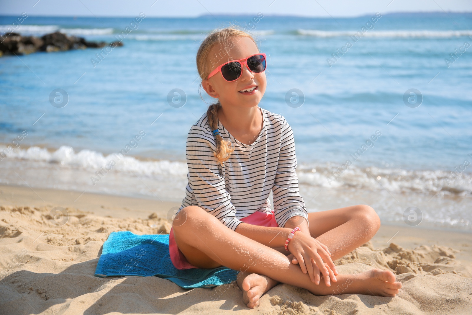 Photo of Happy little girl in stylish sunglasses on sandy beach near sea