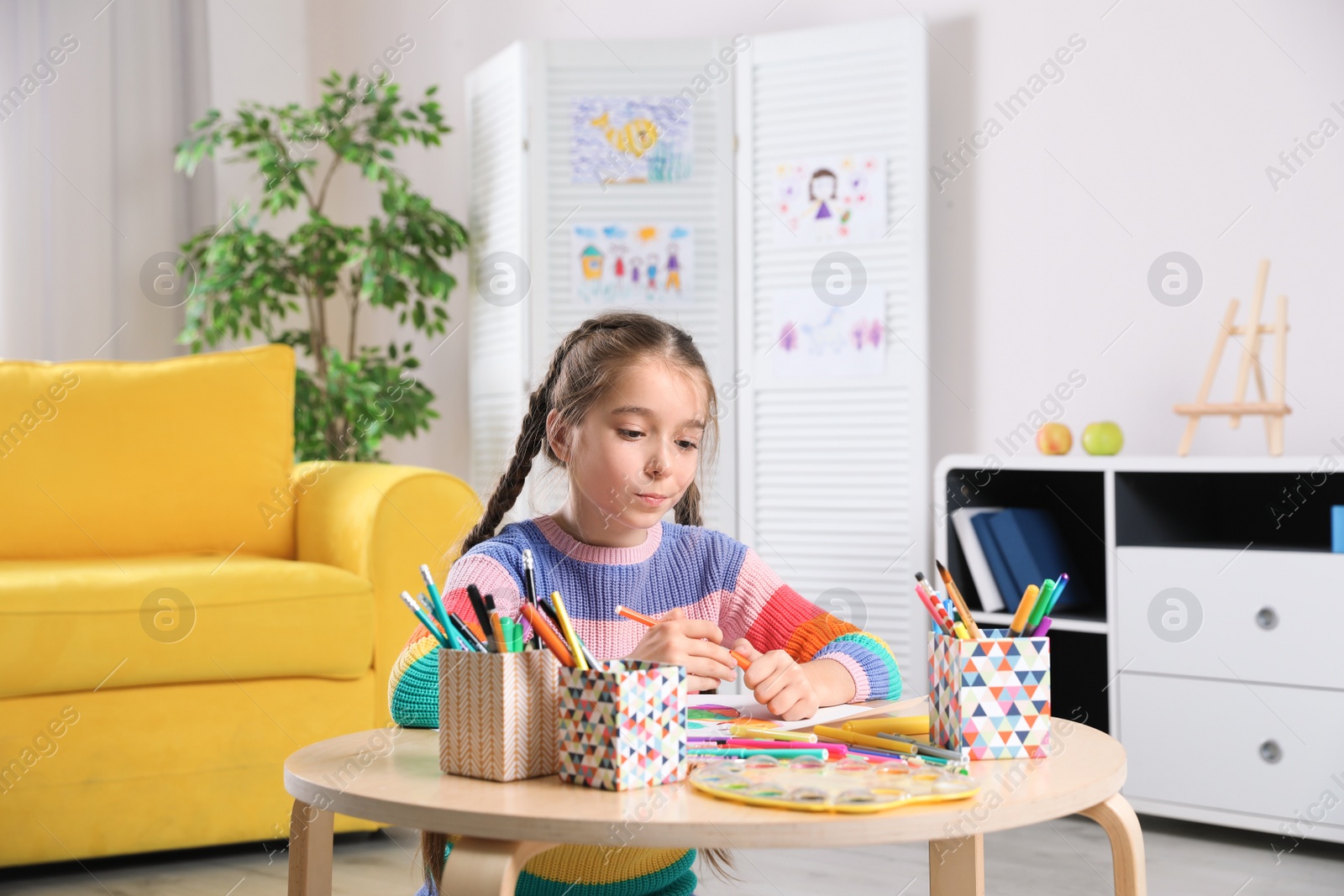 Photo of Little girl drawing picture at table with painting tools indoors