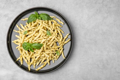 Photo of Plate of delicious trofie pasta with pesto sauce and basil leaves on light grey table, top view. Space for text