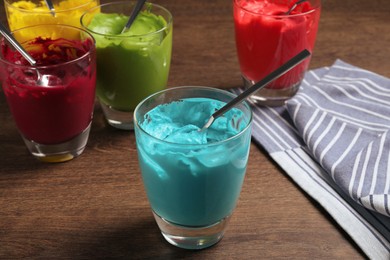 Glasses of different cream with food coloring on wooden table