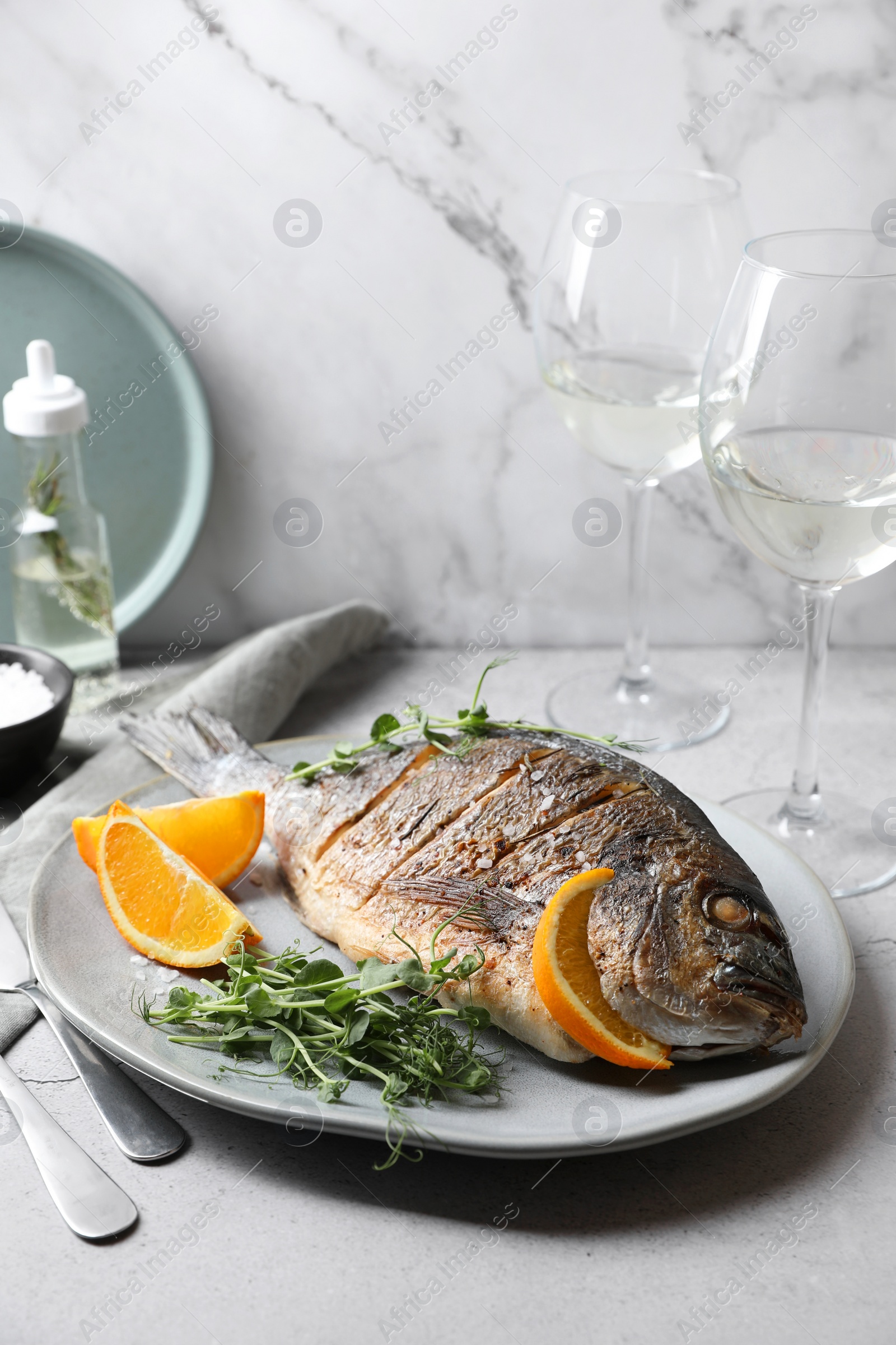 Photo of Seafood. Delicious baked fish served with orange and microgreens on light table