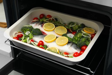 Photo of Raw fish with vegetables and lemon in baking dish into oven indoors