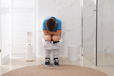 Photo of Boy suffering from hemorrhoid on toilet bowl in rest room