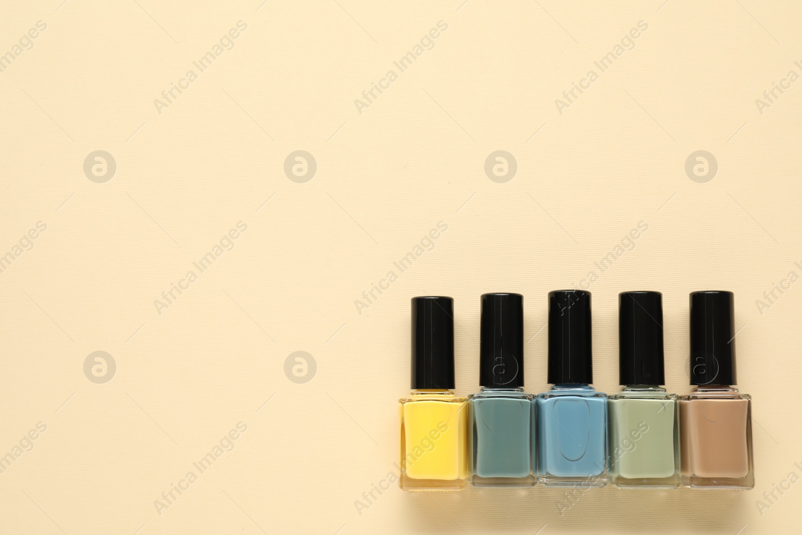 Photo of Bright nail polishes in bottles on beige background, flat lay. Space for text